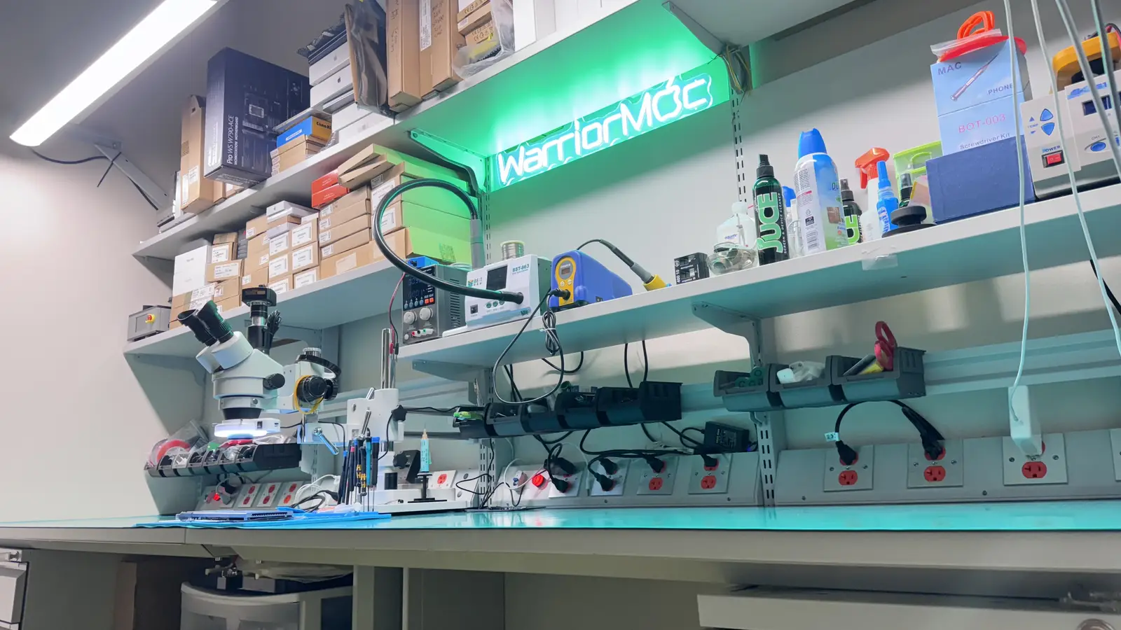 WarriorMac repair workbench with microscope, neon sign, and micro-soldering equipment in Tampa