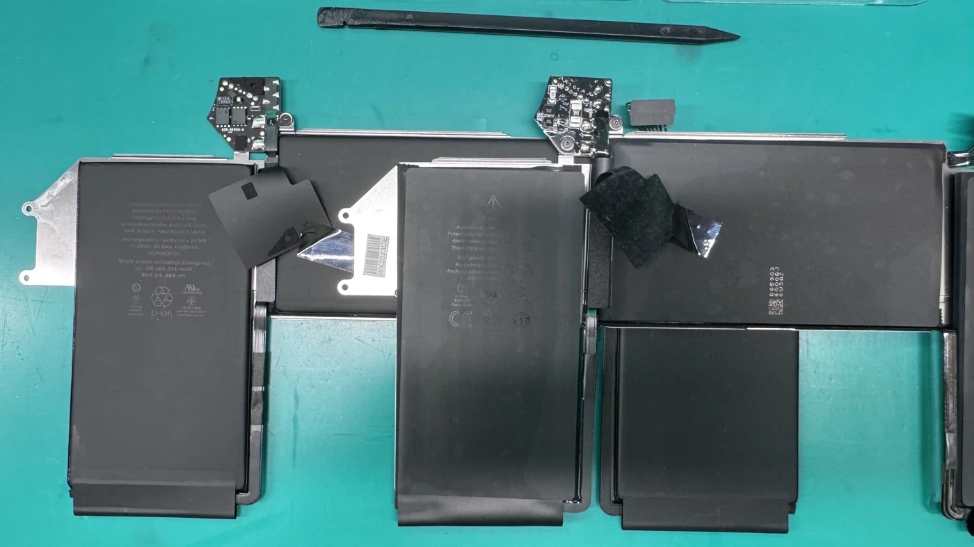 Genuine Apple and counterfeit MacBook Air A2389 batteries laid out with their controller boards on the WarriorMac bench